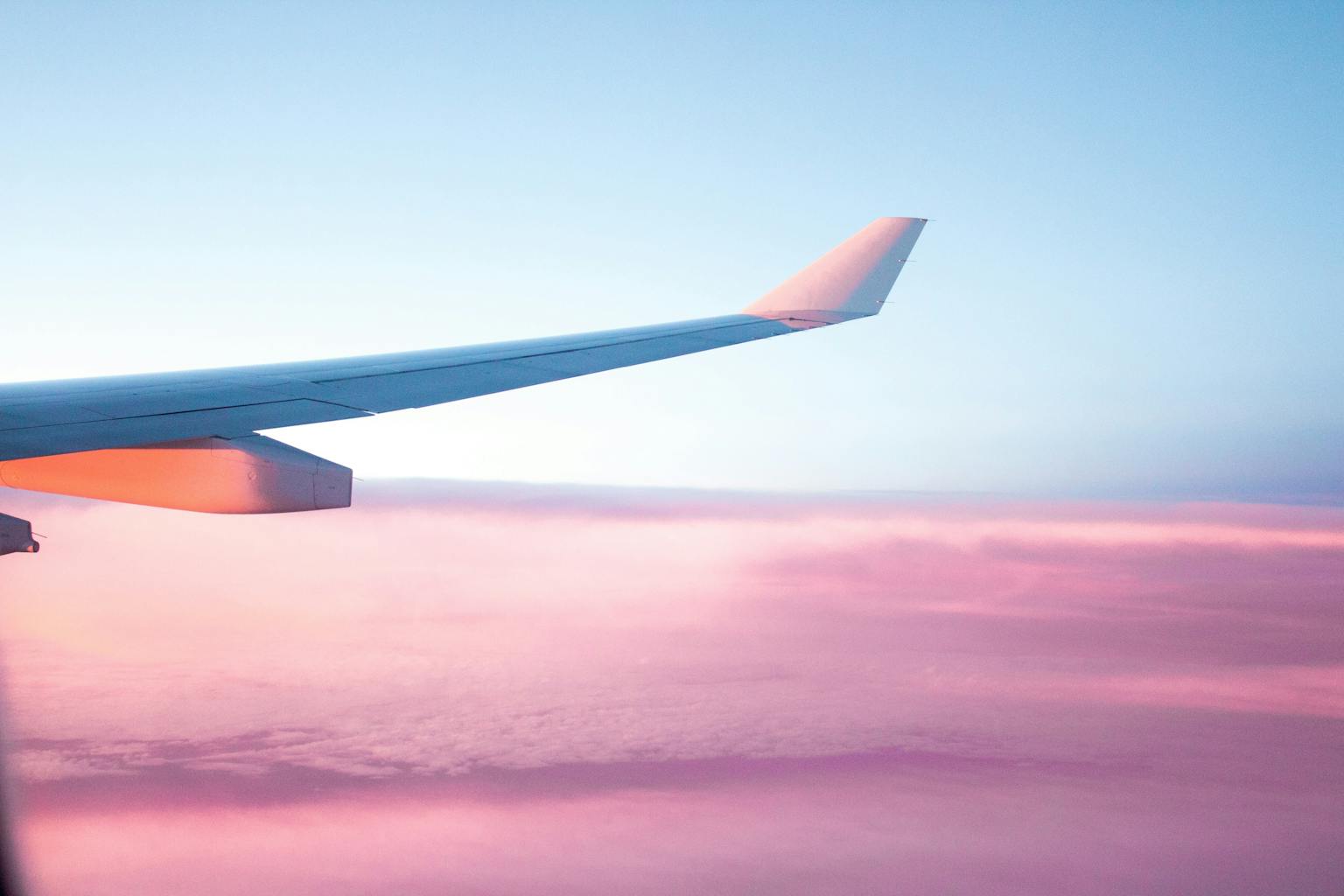 Aile d'avion survolant une mer de nuages roses au coucher de soleil